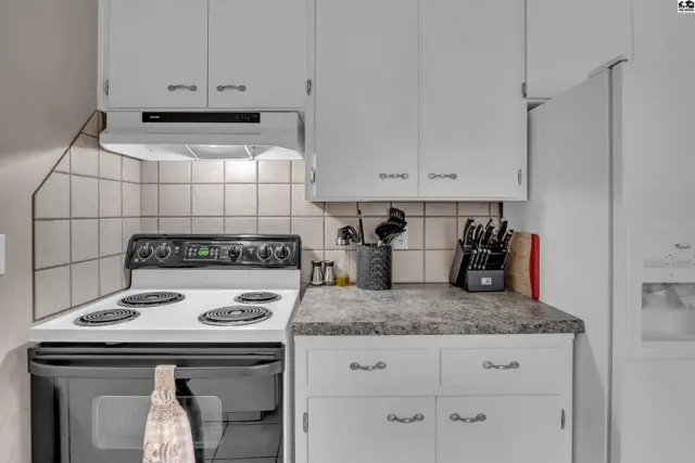 White cabinets and speckled countertops frame a white electric stove and oven.