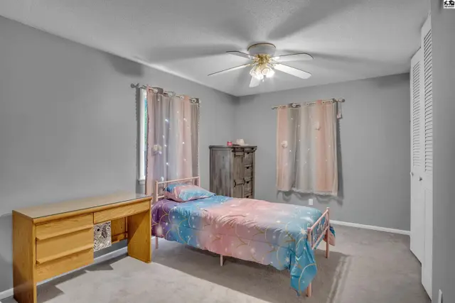 This bedroom features a metal bed frame, a wooden desk, and a ceiling fan.