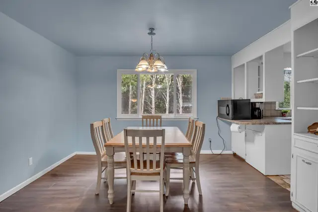 Dining area with wood table, chairs, and a window overlooking trees.