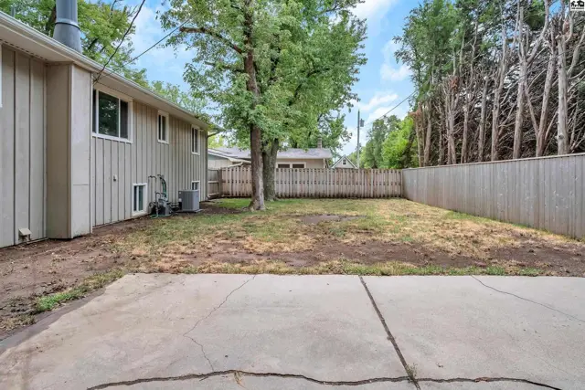 A concrete patio extends into a fenced backyard with mature trees and a detached garage.