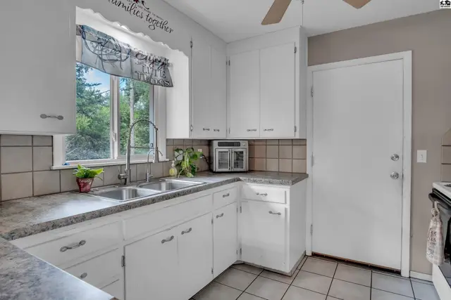 White cabinetry and countertops complement a double sink and tiled backsplash in this kitchen.