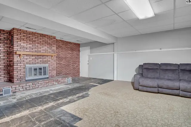 Spacious room features a brick fireplace, carpeted floor, and a partial view of a sofa.