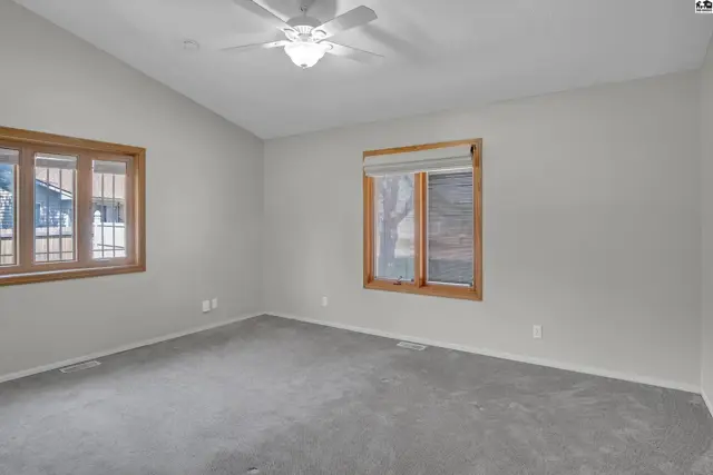 Spacious room with vaulted ceiling, carpeted floor, and two windows.