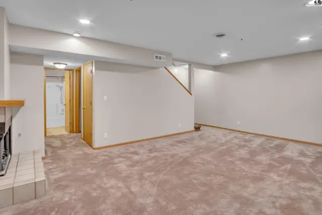 Spacious finished basement with plush carpeting, a fireplace, and access to a bathroom.
