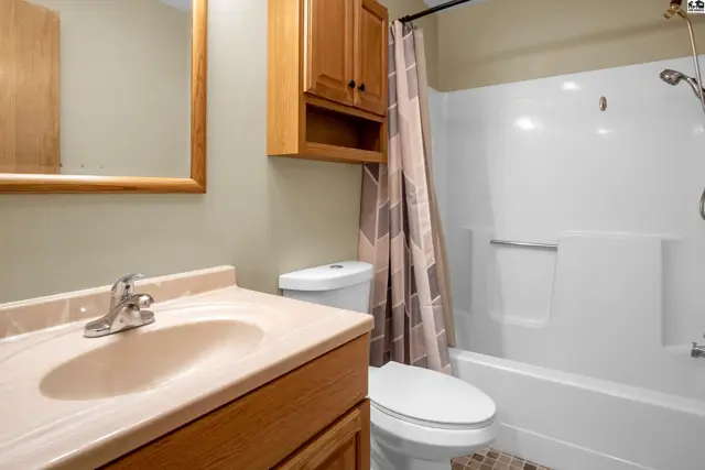 This bathroom features a vanity with a beige countertop, a toilet, and a bathtub with a shower curtain.