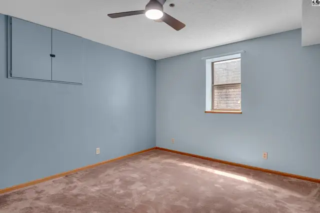 This room features light blue walls, a ceiling fan, and a brown carpeted floor.