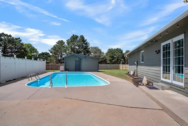 A backyard features a swimming pool, concrete patio, and a detached storage shed.