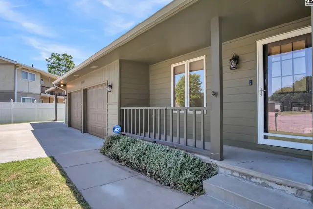 This home features a covered porch with a railing, two garage doors, and a paved driveway.
