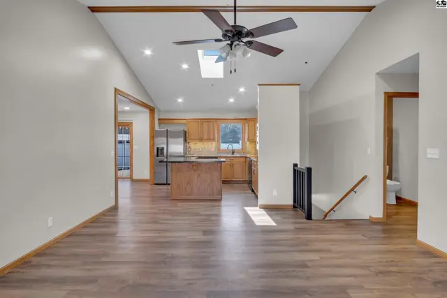 Vaulted ceiling with exposed beams, a ceiling fan, and skylight above an open living area and kitchen.