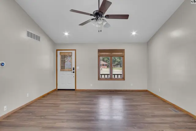 Spacious room with wood-look flooring, a ceiling fan, and a glass-paneled door.