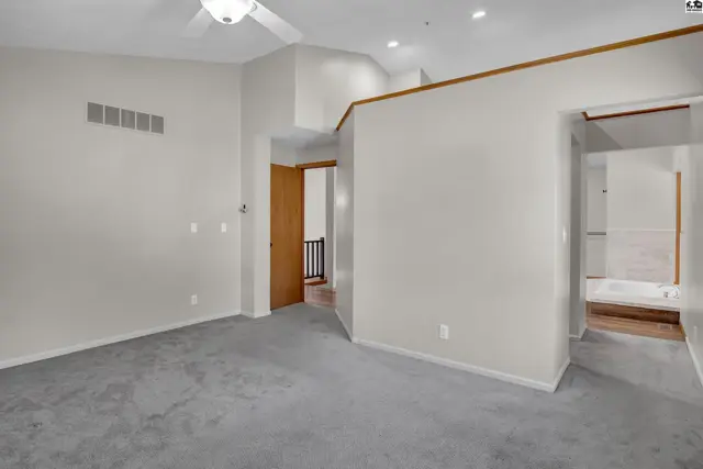 Spacious room with plush grey carpet, vaulted ceiling, and access to a bathroom.
