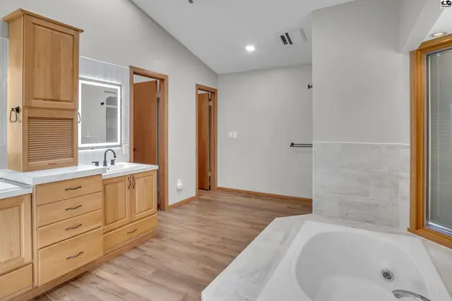 Spacious bathroom features a soaking tub, double vanity with wood cabinetry, and tiled shower enclosure.
