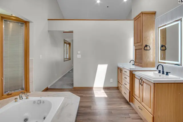 Spacious bathroom features a soaking tub, dual vanities, and ample wood cabinetry.
