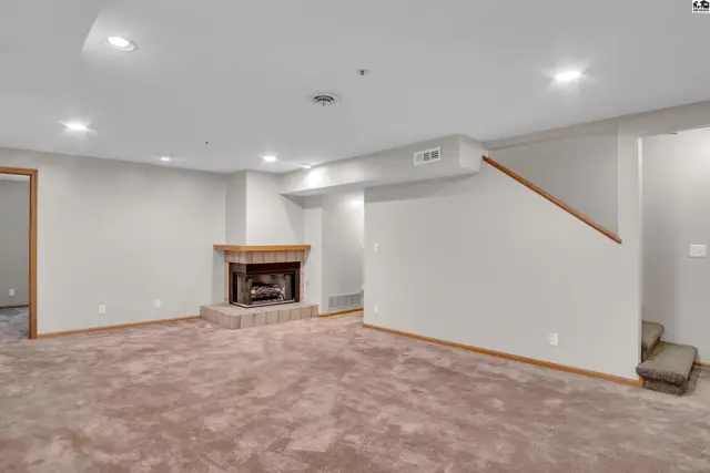 Spacious room with carpet, a brick fireplace, and access to stairs.
