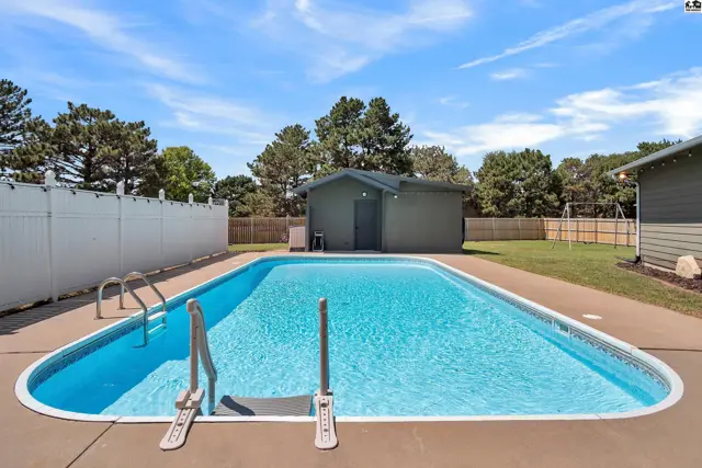 Rectangular swimming pool with metal ladder and deck surrounded by a white fence and green lawn.