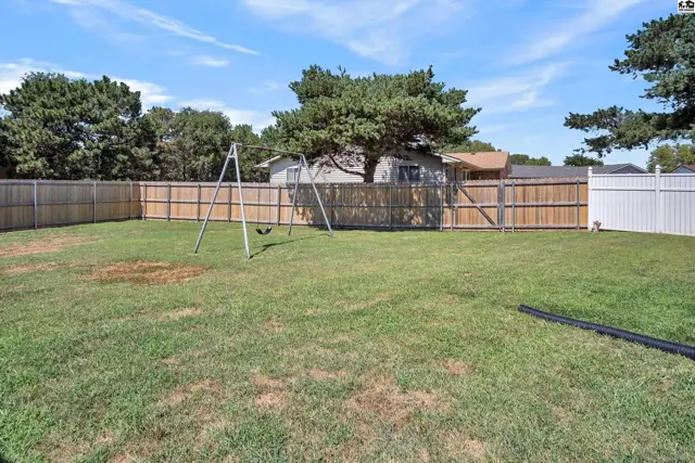 Spacious fenced backyard with a swing set and mature trees.