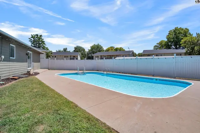 Inground swimming pool with concrete deck and white vinyl fencing.