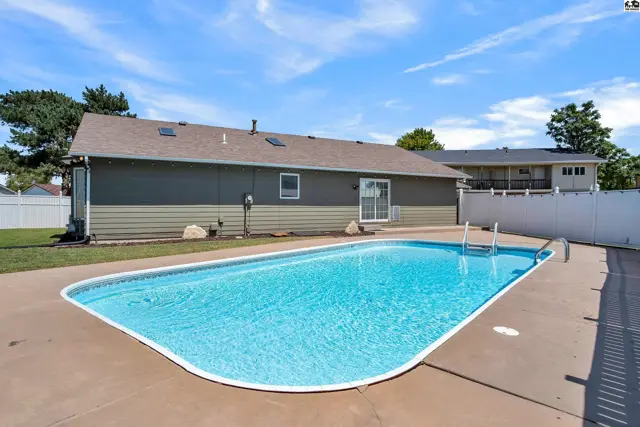 Inground swimming pool with concrete surround and a fenced backyard.