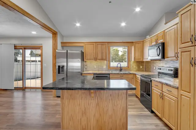 This kitchen features light wood cabinetry, granite countertops, and stainless steel appliances.