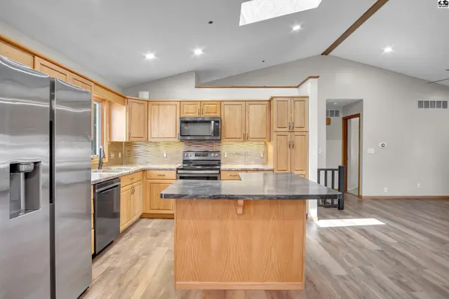 Spacious kitchen features light wood cabinetry, granite countertops, and a central island.