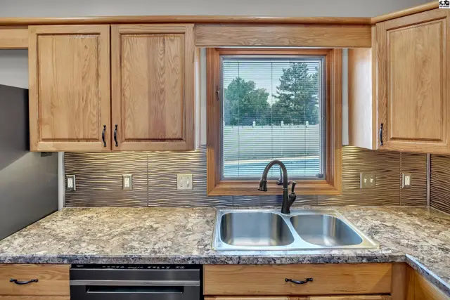 Kitchen features oak cabinetry, granite countertops, a double sink, and a tiled backsplash.
