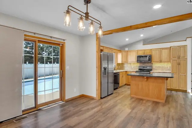 This kitchen features light wood cabinetry, a central island, and stainless steel appliances.