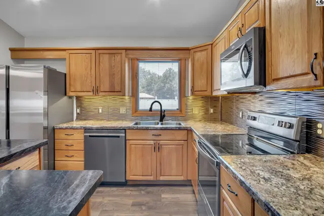 This kitchen features light wood cabinetry, granite countertops, and stainless steel appliances.