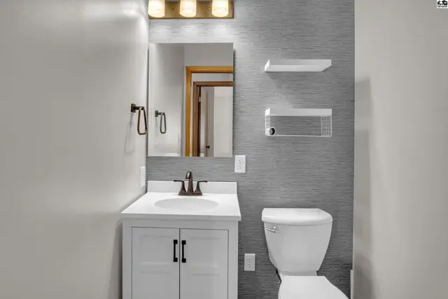 This bathroom features a white vanity, toilet, and a textured grey accent wall.