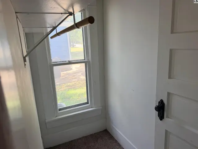 This small room features a window, a closet rod, and a paneled door.