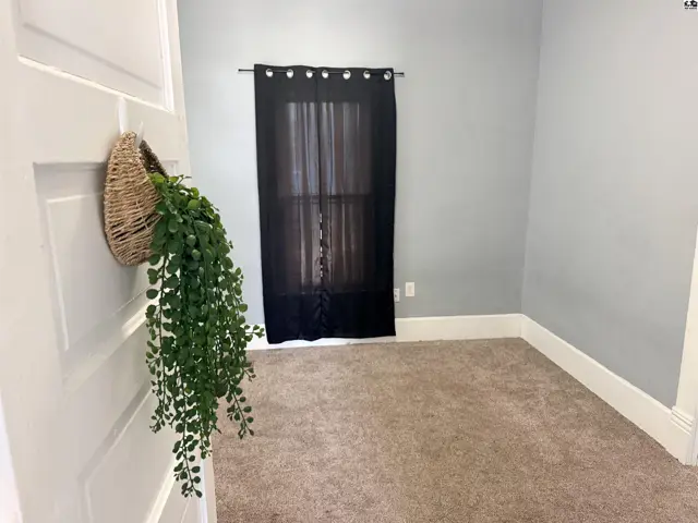 This room features neutral carpet, light grey walls, and a black curtained window.