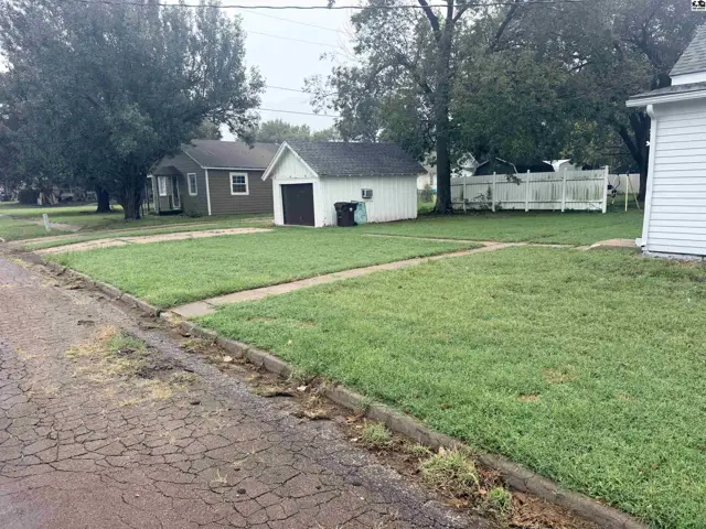 A white detached garage with a dark door sits on a grassy lot with a white fence.