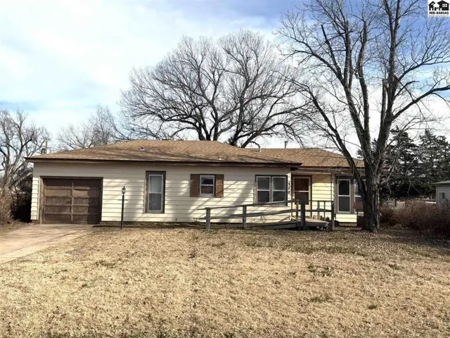 This single-story home features a light-colored exterior, attached garage, and a sloped driveway.
