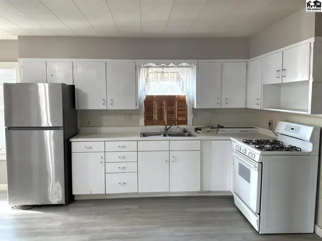 White cabinets and countertops line the walls of this kitchen, featuring a stainless steel refrigerator and a gas range.