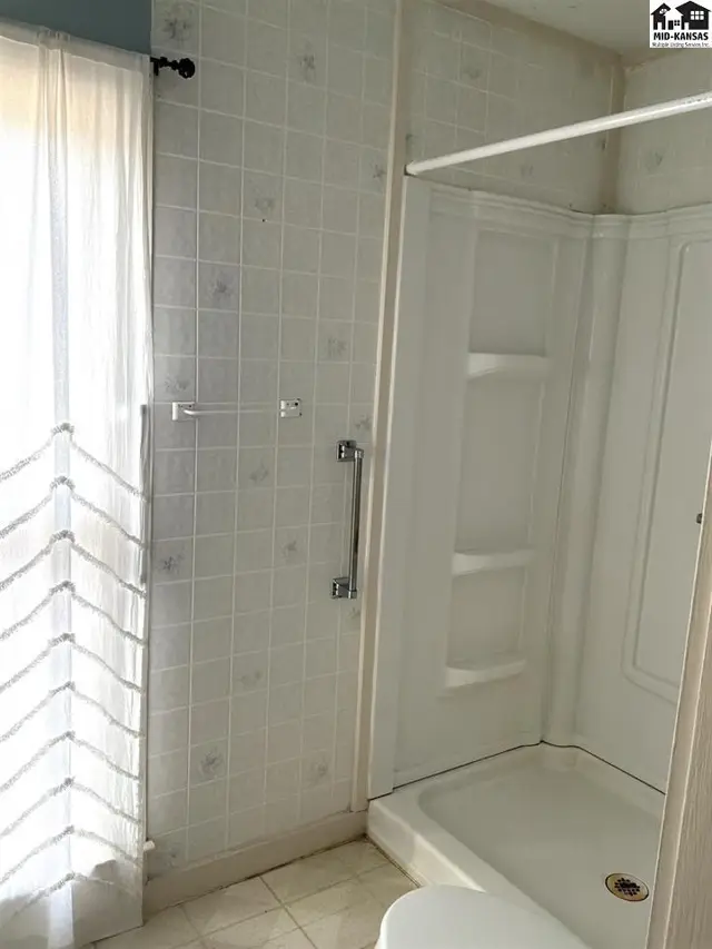 White tiled walls surround a shower stall with built-in shelving.
