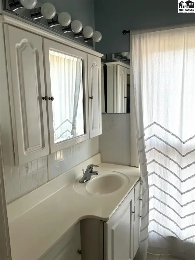 White vanity with a sink, mirror, and tiled backsplash is illuminated by a light fixture.