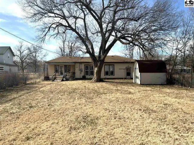 Single-story home with a large yard, mature tree, and detached storage shed.
