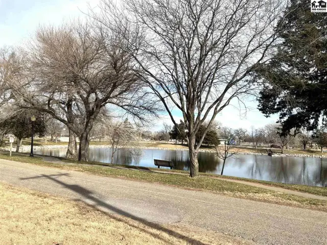 A paved path winds past bare trees and a tranquil pond with a bench.