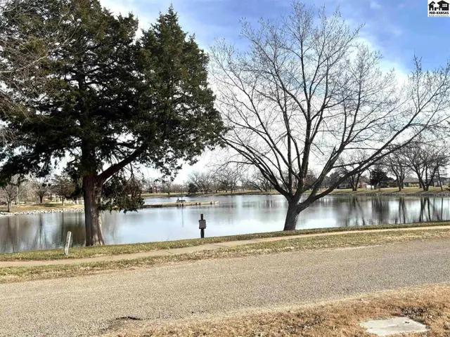 A paved path borders a tranquil lake with mature trees and open grassy areas.