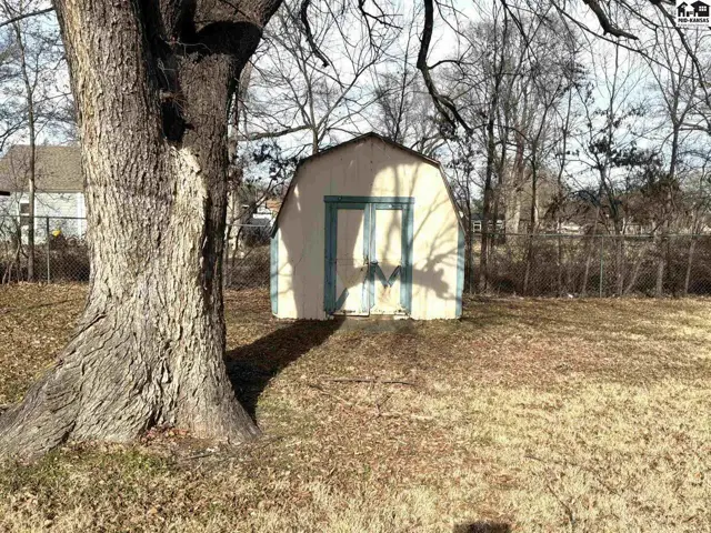 A small, light-colored shed with a double door sits on a grassy yard.