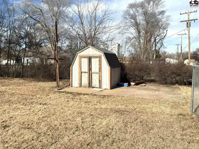 A small, white shed with double doors sits on a concrete pad in a dry, grassy yard.