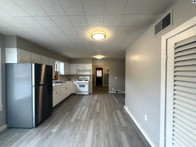 Spacious kitchen with white cabinetry, stainless steel refrigerator, and light grey wood-look flooring.