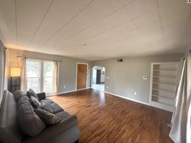 Spacious living room with hardwood floors, a large window, and built-in shelving.
