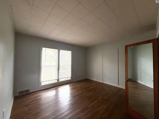 Spacious room with hardwood floors, large windows, and a mirrored closet door.