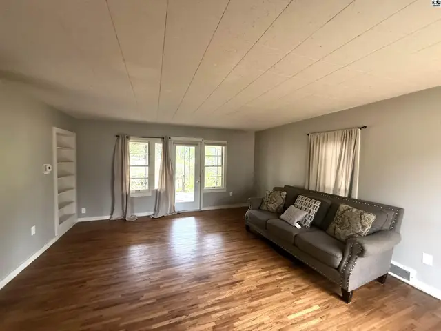 Spacious living room with hardwood floors, built-in shelving, and large windows.