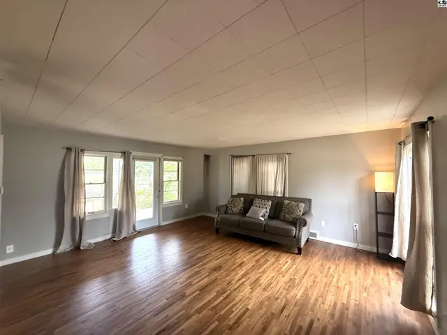 Spacious living room with hardwood floors, large windows, and a glass door.
