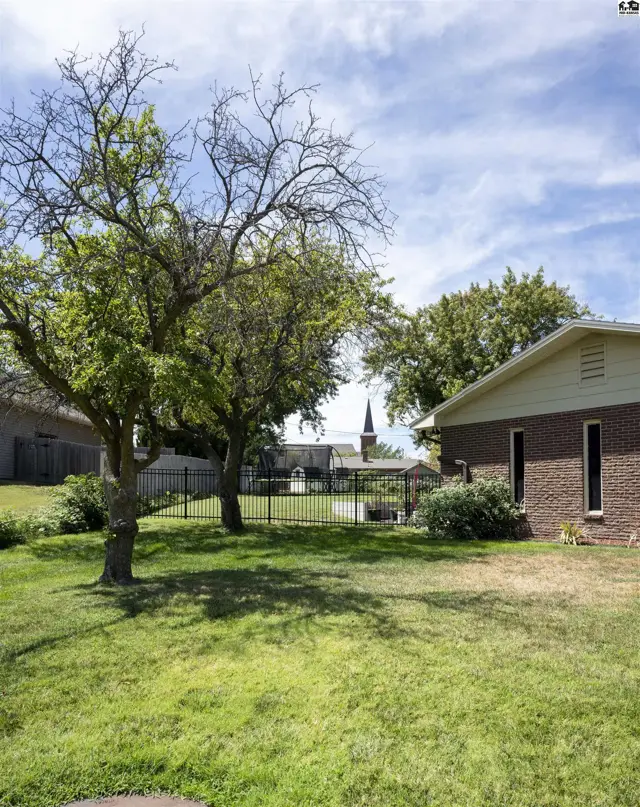 Brick home with a fenced yard and mature trees under a partly cloudy sky.