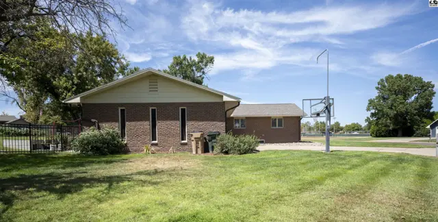 Brick home with a basketball hoop and mature trees on a grassy lot.