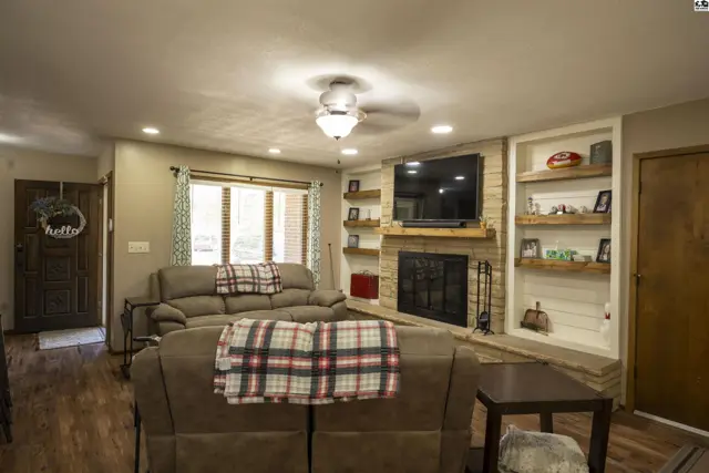 Spacious living room features a brick fireplace, built-in shelving, and a ceiling fan.