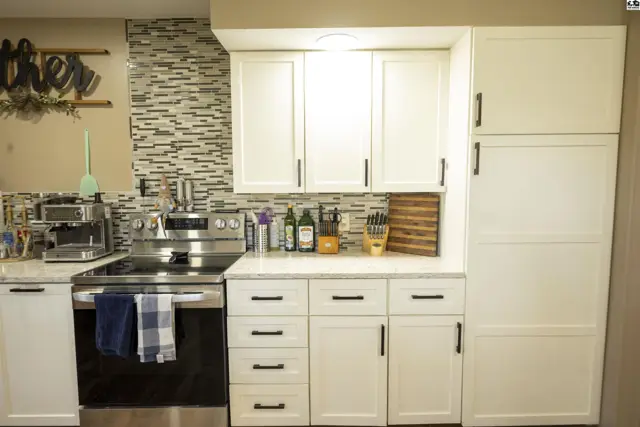 White cabinetry with black hardware complements a stainless steel range and mosaic tile backsplash.