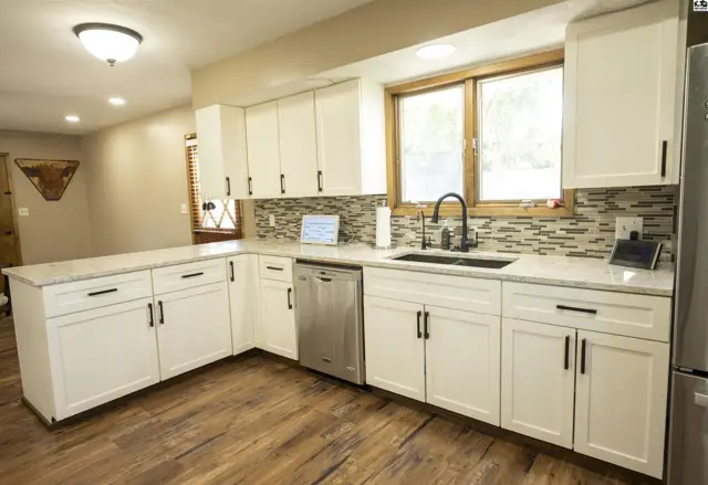 White cabinetry, granite countertops, and a mosaic tile backsplash accent this spacious kitchen.